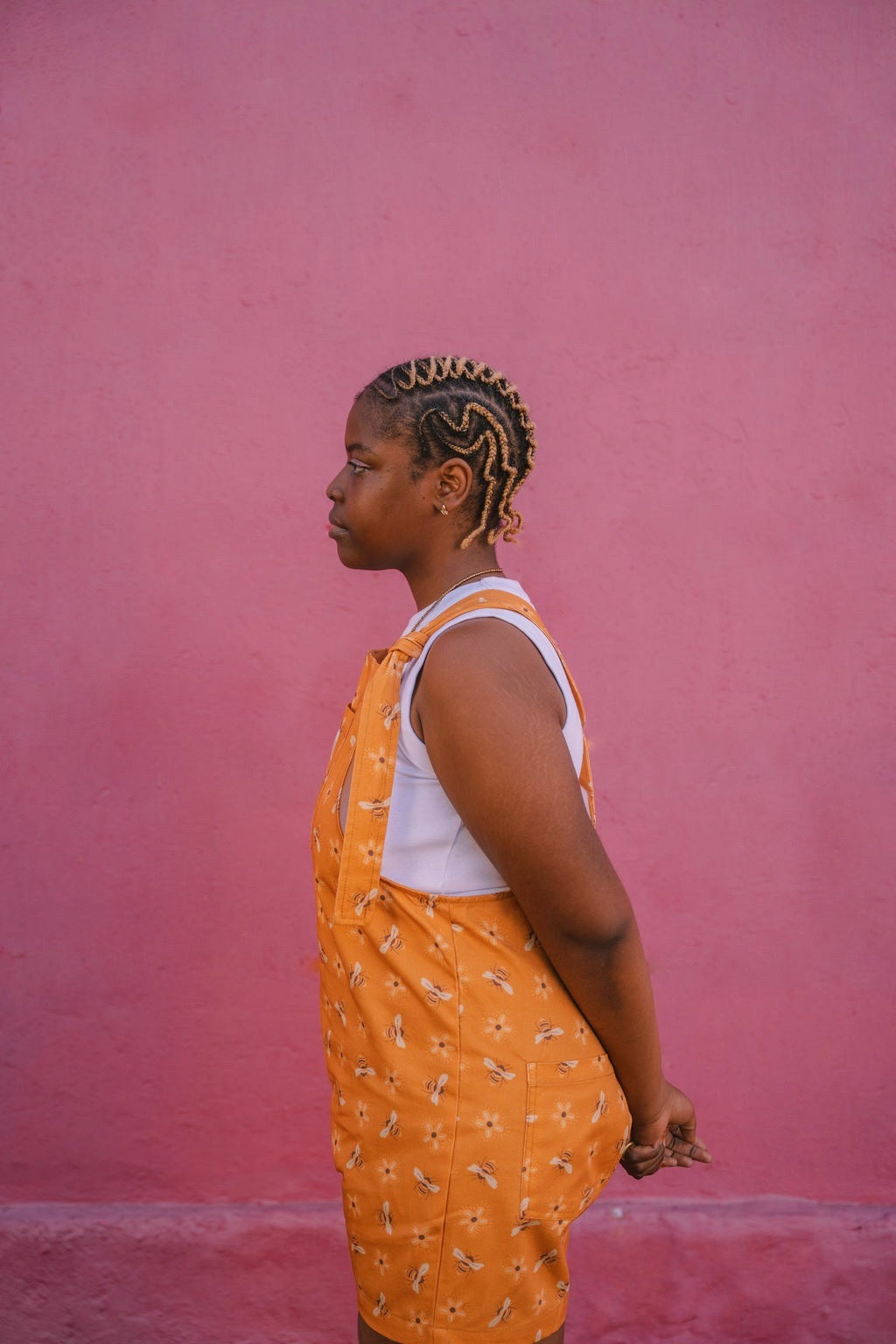 Person wearing orange, yellow mustard, bees patterned dungarees/ overalls against a pink wall size L