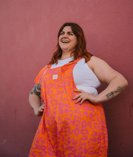 Person wearing size XXL orange and pink patterned Lamps overalls/dungarees standing against a pink wall.