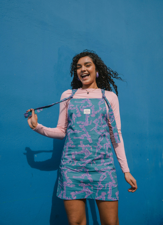 Woman wearing a blue and purple funky patterned dungaree/overall dress against a blue background