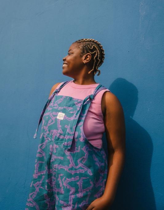Person wearing a blue, purple patterned dungarees/overalls size Large with a pink crop top against a blue background