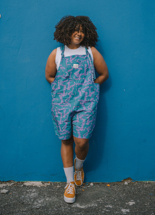 Person wearing a colorful patterned overalls dungarees against a blue wall