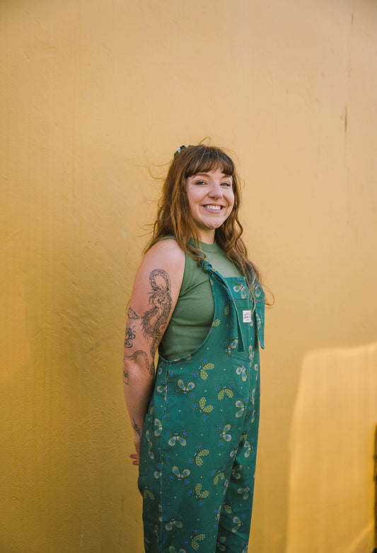 Person wearing green Butterfly long patterned overalls/dungarees against a yellow wall