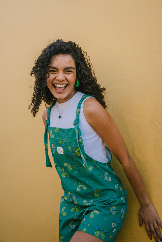 Woman wearing green patterned overalls/dungarees with butterfly's against a yellow wall