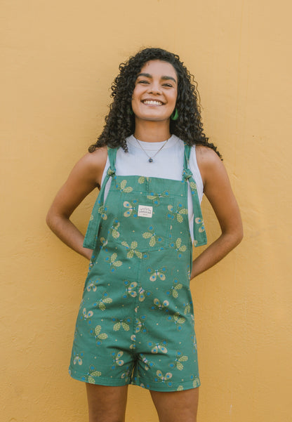Woman wearing green patterned overalls/dungarees with butterfly's against a yellow wall