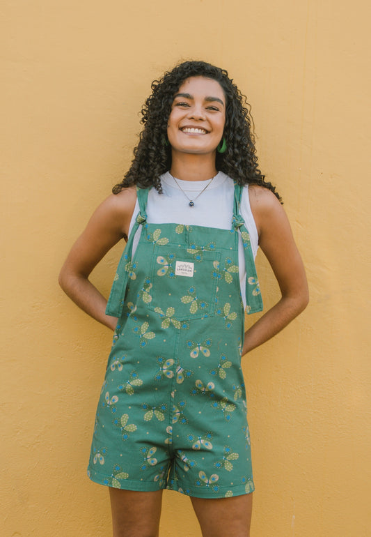 Woman wearing green patterned overalls/dungarees with butterfly's against a yellow wall
