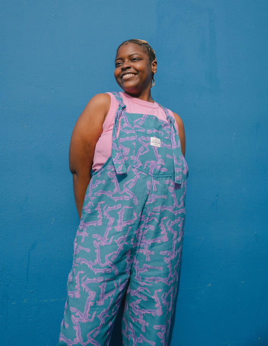 Person wearing a blue, purple, pink  patterned dungarees/overalls size Large against a blue background