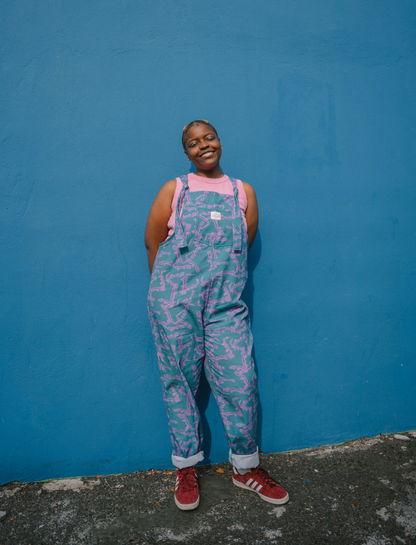 Person wearing a blue, purple patterned dungarees/overalls size Large with a pink crop top against a blue background