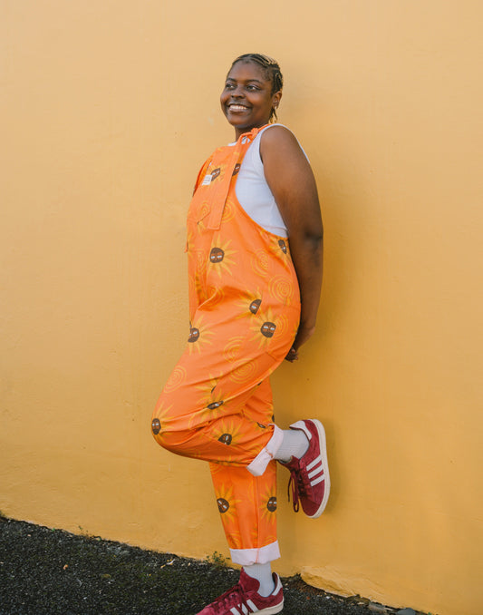 Person wearing an orange sunflower patterned dungaree & overall against a yellow wall