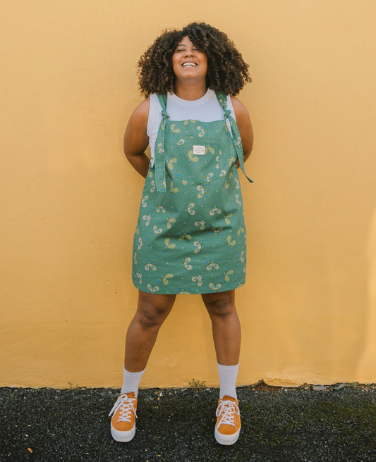 Person wearing a green butterfly patterned dungaree with dress against a yellow wall