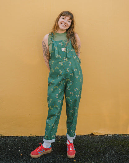 Person wearing green Butterfly long patterned overalls/dungarees against a yellow wall